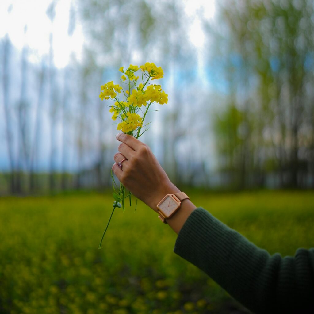 Close-up of hand wearing a watch holding yellow wildflowers outdoors in spring.